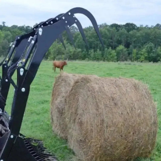 Top Dog Attachments skid steer bale grapple next to round hay bales in a pasture